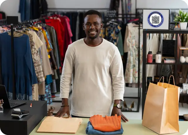 A smiling merchant behind the counter of their clothing shop